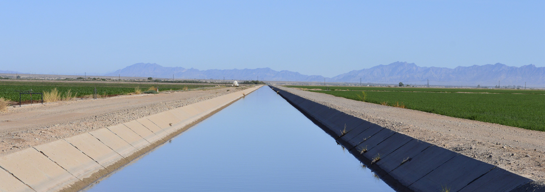 Large irrigation canal filled with water between two agricultural fields near Blythe, California.